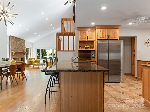 kitchen featuring a breakfast bar area, freestanding refrigerator, a brick fireplace, a sink, and dark stone countertops