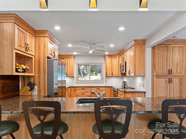 kitchen with a peninsula, a breakfast bar area, stainless steel appliances, and dark stone countertops