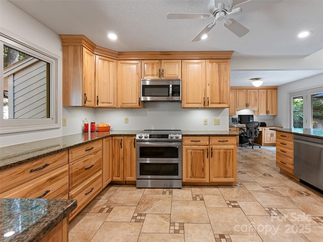 kitchen featuring built in desk, stainless steel appliances, recessed lighting, a textured ceiling, and dark stone counters