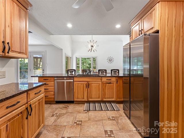 kitchen featuring dark stone counters, appliances with stainless steel finishes, a sink, and a healthy amount of sunlight