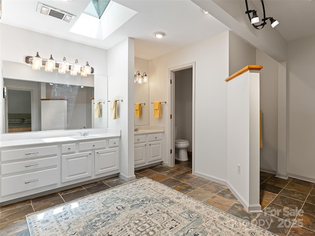 full bath with stone tile floors, visible vents, toilet, a sink, and two vanities