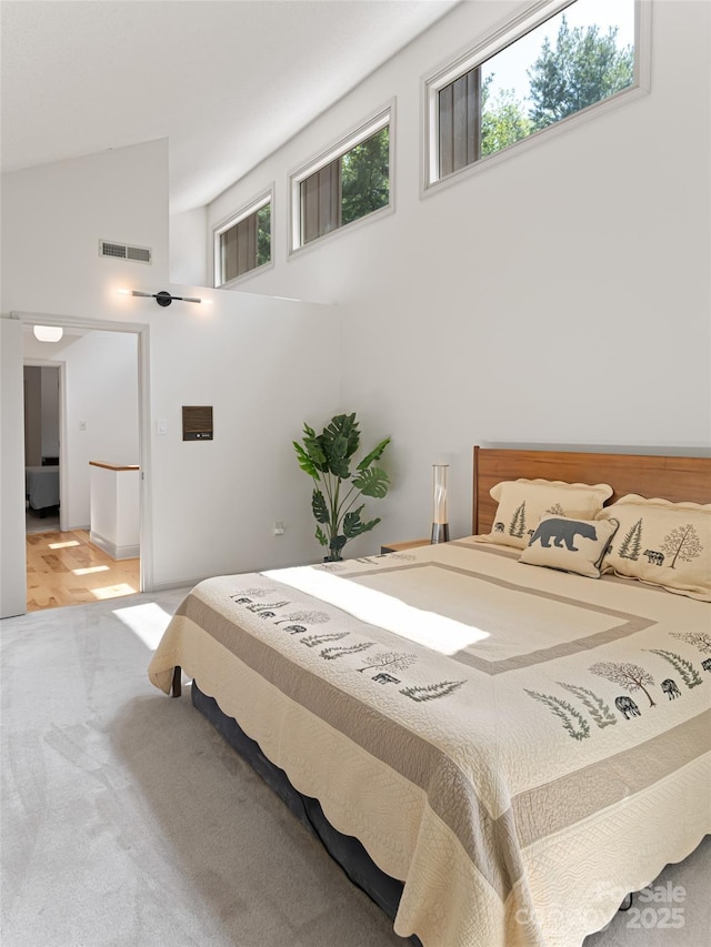 carpeted bedroom with high vaulted ceiling, multiple windows, and visible vents