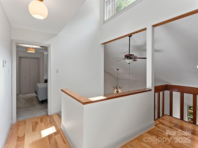 corridor with wood finished floors, an upstairs landing, and baseboards