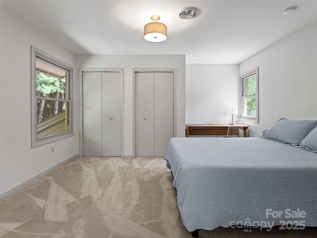 bedroom with two closets, visible vents, and light colored carpet