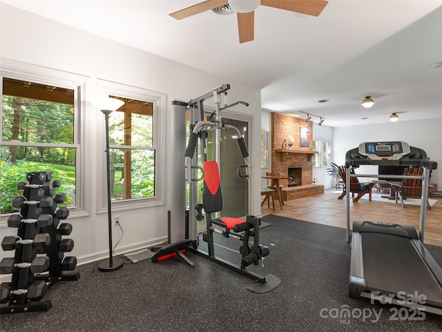 exercise area with a brick fireplace, baseboards, and a ceiling fan