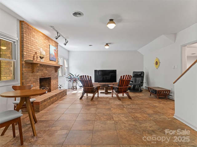 living room featuring a brick fireplace, visible vents, and track lighting