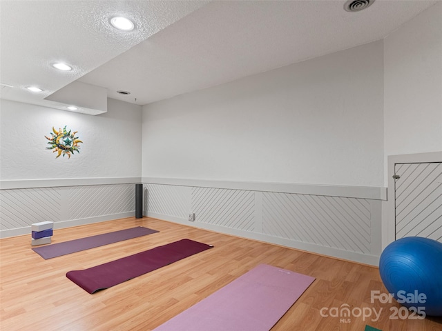 exercise room with a wainscoted wall, recessed lighting, visible vents, a textured ceiling, and wood finished floors