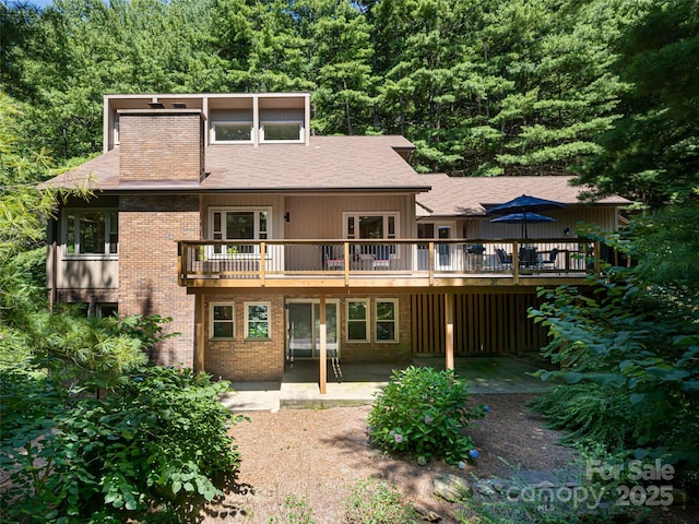 rear view of house with a shingled roof, brick siding, a patio, and a deck