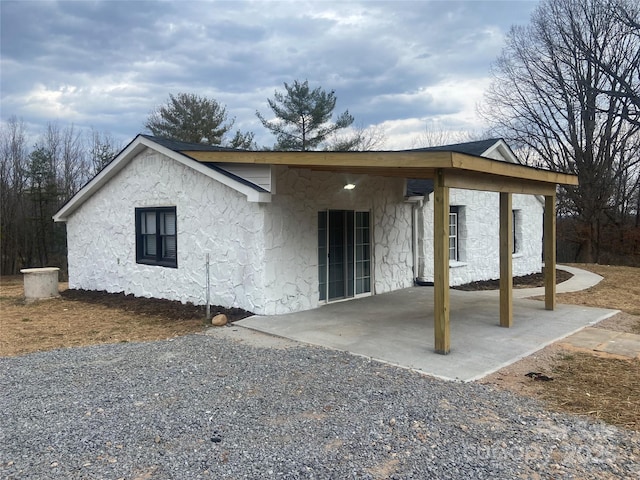 view of front of house featuring a patio area, gravel driveway, and stucco siding