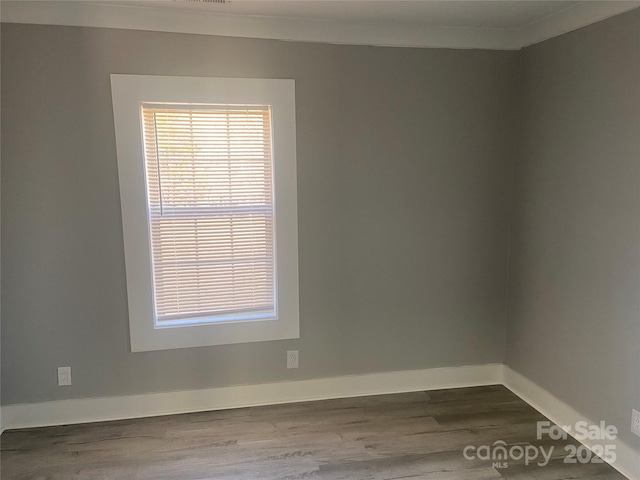 unfurnished room featuring dark wood-style floors, ornamental molding, and baseboards