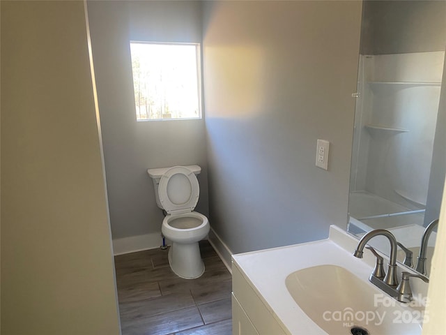 bathroom with baseboards, toilet, walk in shower, vanity, and wood finish floors