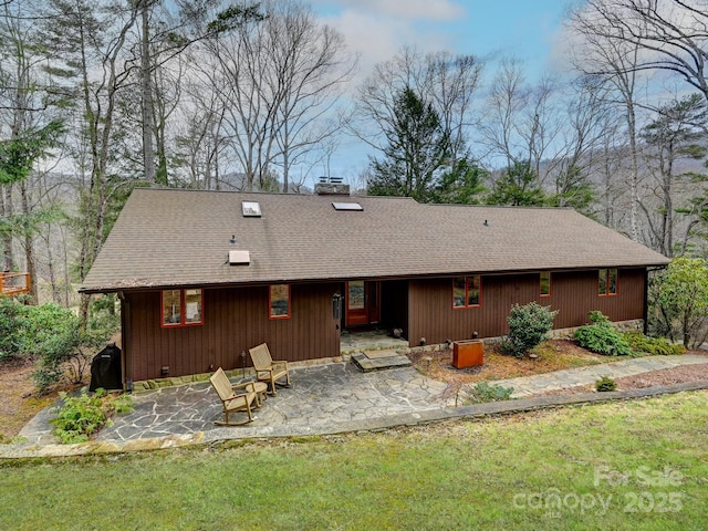 view of front of house with a chimney, roof with shingles, a patio area, and a front yard