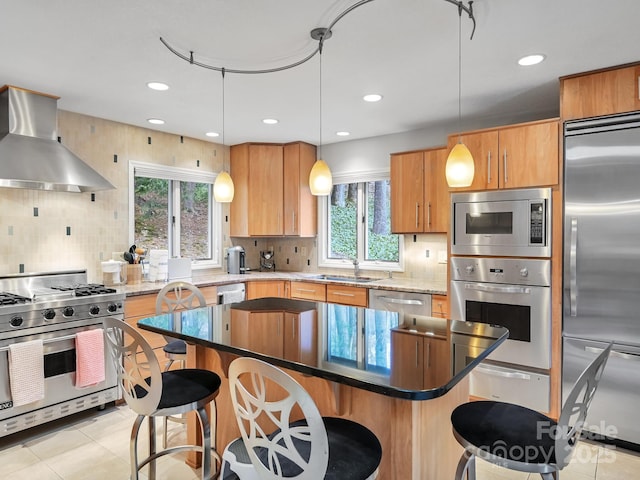 kitchen featuring range hood, a breakfast bar area, hanging light fixtures, a sink, and built in appliances