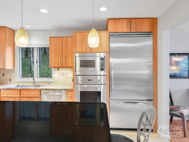 kitchen featuring decorative light fixtures, decorative backsplash, a sink, light stone countertops, and built in appliances