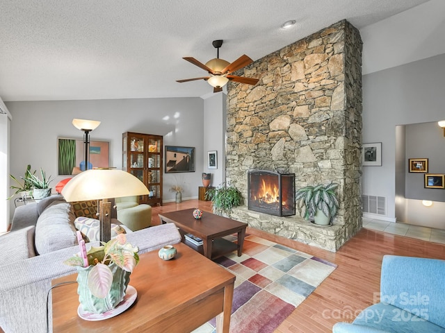 living room featuring a textured ceiling, a fireplace, wood finished floors, visible vents, and a ceiling fan