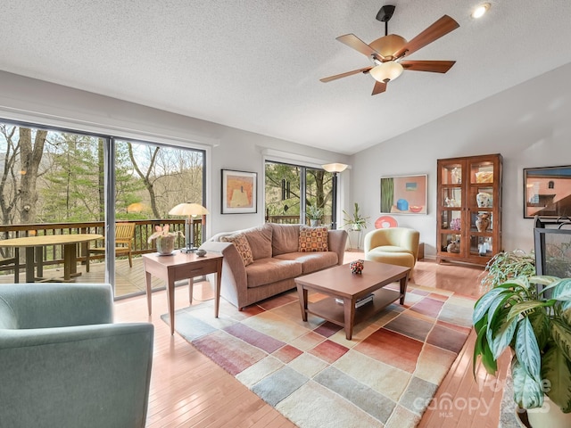 living room featuring light wood-type flooring, vaulted ceiling, a textured ceiling, and ceiling fan