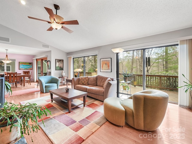 living area featuring light wood-style floors, lofted ceiling, visible vents, and a textured ceiling