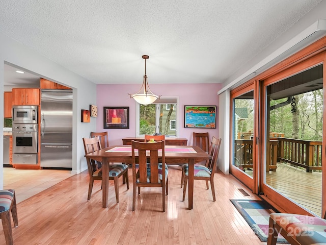 dining area featuring light wood-type flooring, a textured ceiling, visible vents, and a wealth of natural light