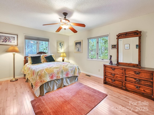 bedroom with visible vents, a ceiling fan, a textured ceiling, baseboards, and hardwood / wood-style flooring