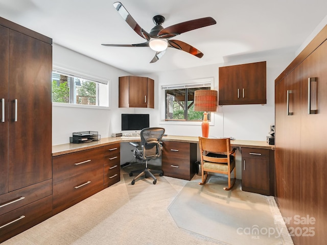 office space with ceiling fan, light carpet, and built in study area