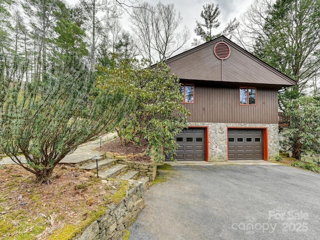 view of side of home with an attached garage, stone siding, and aphalt driveway