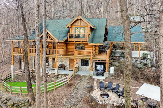 exterior space with an outdoor fire pit, log exterior, a balcony, stone siding, and a patio area