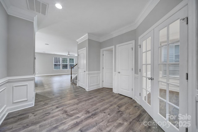 spare room featuring visible vents, a wainscoted wall, stairway, ornamental molding, and wood finished floors