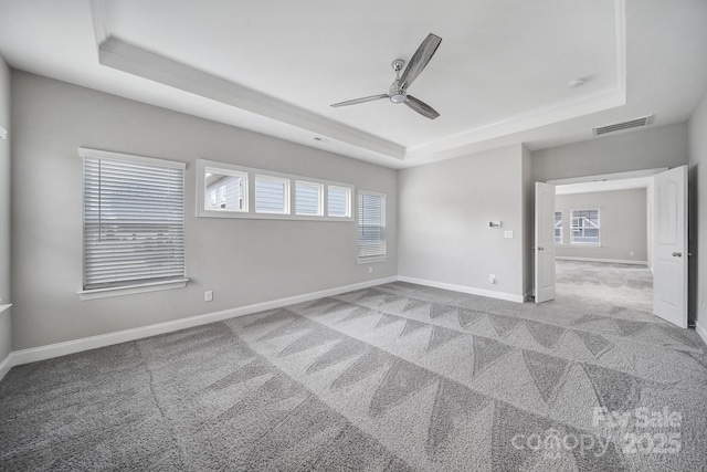 spare room featuring a raised ceiling, light colored carpet, visible vents, and baseboards