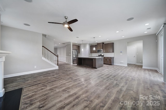 unfurnished living room featuring ceiling fan, recessed lighting, wood finished floors, baseboards, and stairway