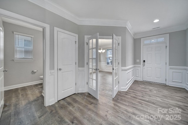 foyer entrance featuring wainscoting, wood finished floors, visible vents, and crown molding