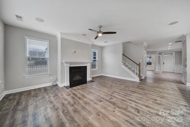 unfurnished living room with wood finished floors, stairway, a fireplace with flush hearth, and visible vents