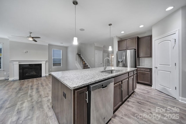 kitchen featuring light wood-style flooring, appliances with stainless steel finishes, a glass covered fireplace, a sink, and dark brown cabinets