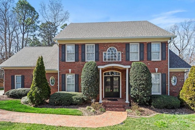 colonial house with brick siding, french doors, and a shingled roof