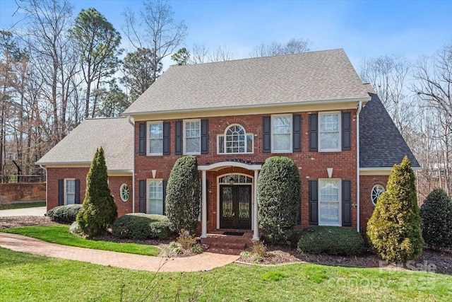 colonial-style house with french doors, brick siding, a front lawn, and roof with shingles