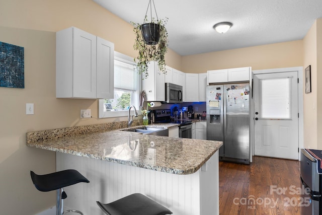 kitchen with a peninsula, a sink, white cabinets, appliances with stainless steel finishes, and light stone countertops