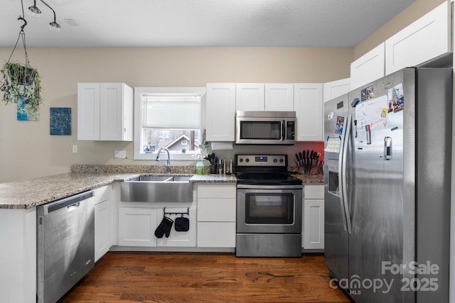 kitchen featuring a peninsula, appliances with stainless steel finishes, a sink, and white cabinets