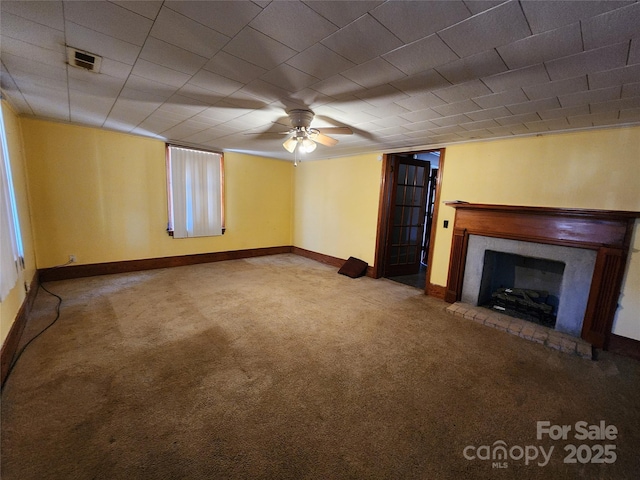 unfurnished living room featuring visible vents, baseboards, a ceiling fan, a fireplace with raised hearth, and carpet flooring