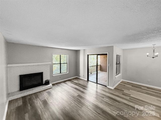 unfurnished living room featuring a brick fireplace, a textured ceiling, wood finished floors, a chandelier, and baseboards