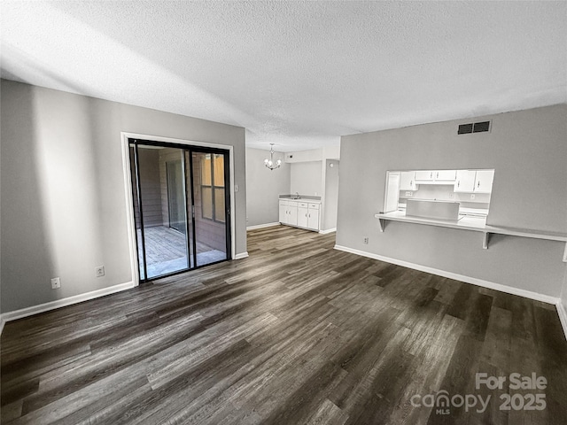 unfurnished living room featuring visible vents, dark wood-type flooring, a textured ceiling, a chandelier, and baseboards