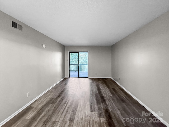 empty room with dark wood finished floors, visible vents, and baseboards