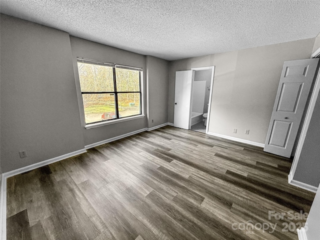 unfurnished bedroom featuring ensuite bathroom, a textured ceiling, baseboards, and wood finished floors