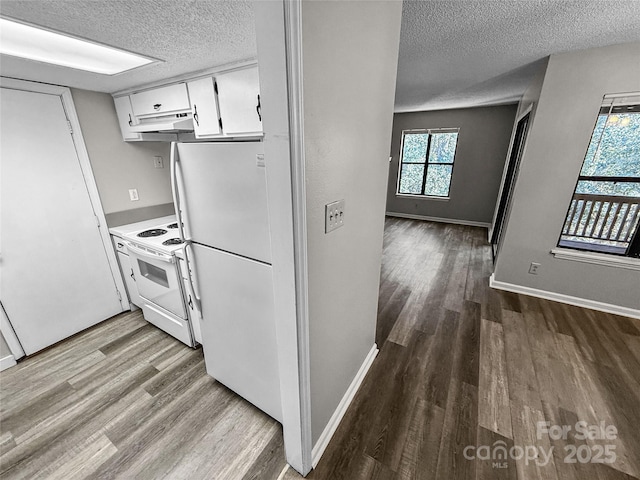 kitchen featuring white appliances, wood finished floors, a textured ceiling, under cabinet range hood, and white cabinetry