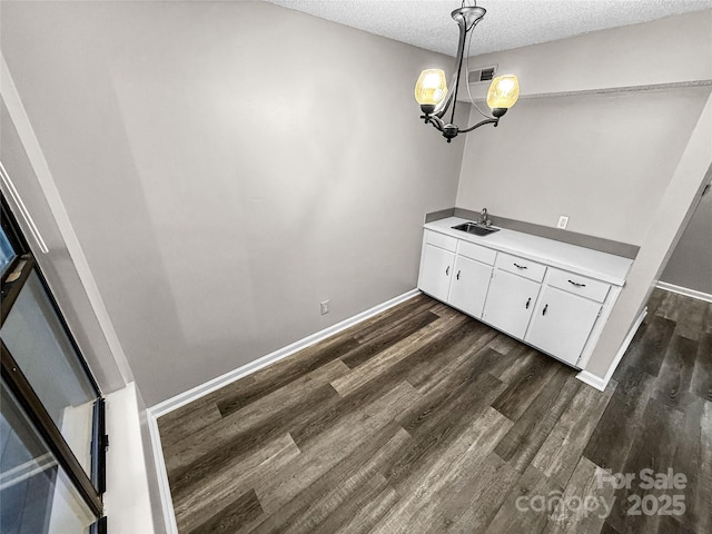 unfurnished dining area featuring visible vents, dark wood-type flooring, a sink, a textured ceiling, and baseboards