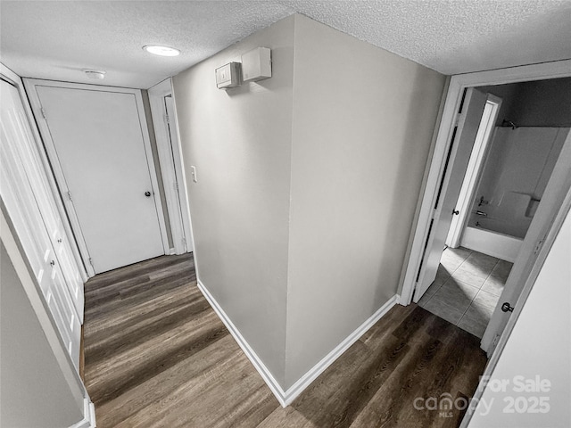 hallway featuring baseboards, dark wood finished floors, and a textured ceiling