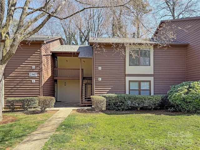 view of front of house featuring roof with shingles, a front lawn, and stairs