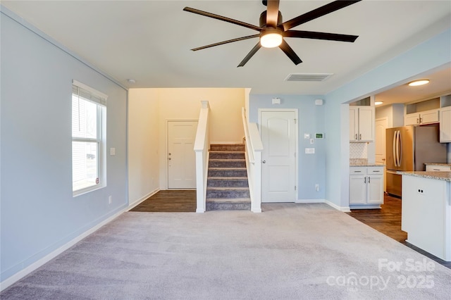 unfurnished living room with visible vents, stairway, carpet floors, baseboards, and ceiling fan