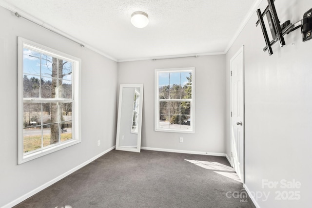 spare room featuring a textured ceiling, ornamental molding, dark carpet, and baseboards