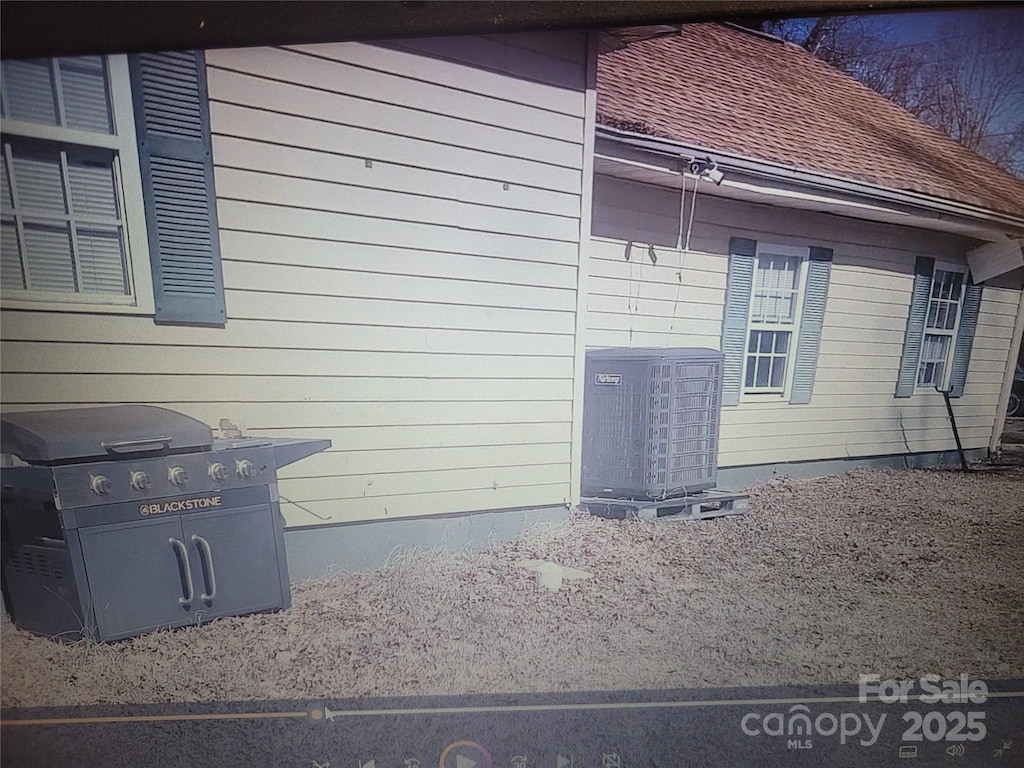 view of side of property featuring central AC and roof with shingles