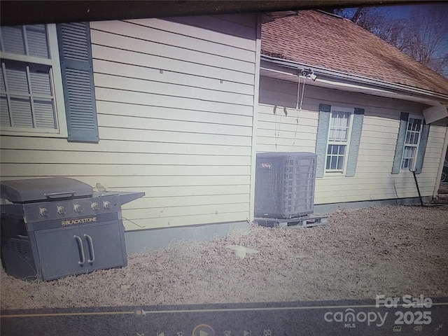 view of side of property featuring central AC and roof with shingles