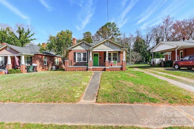 bungalow with a porch, brick siding, a carport, a front lawn, and a chimney